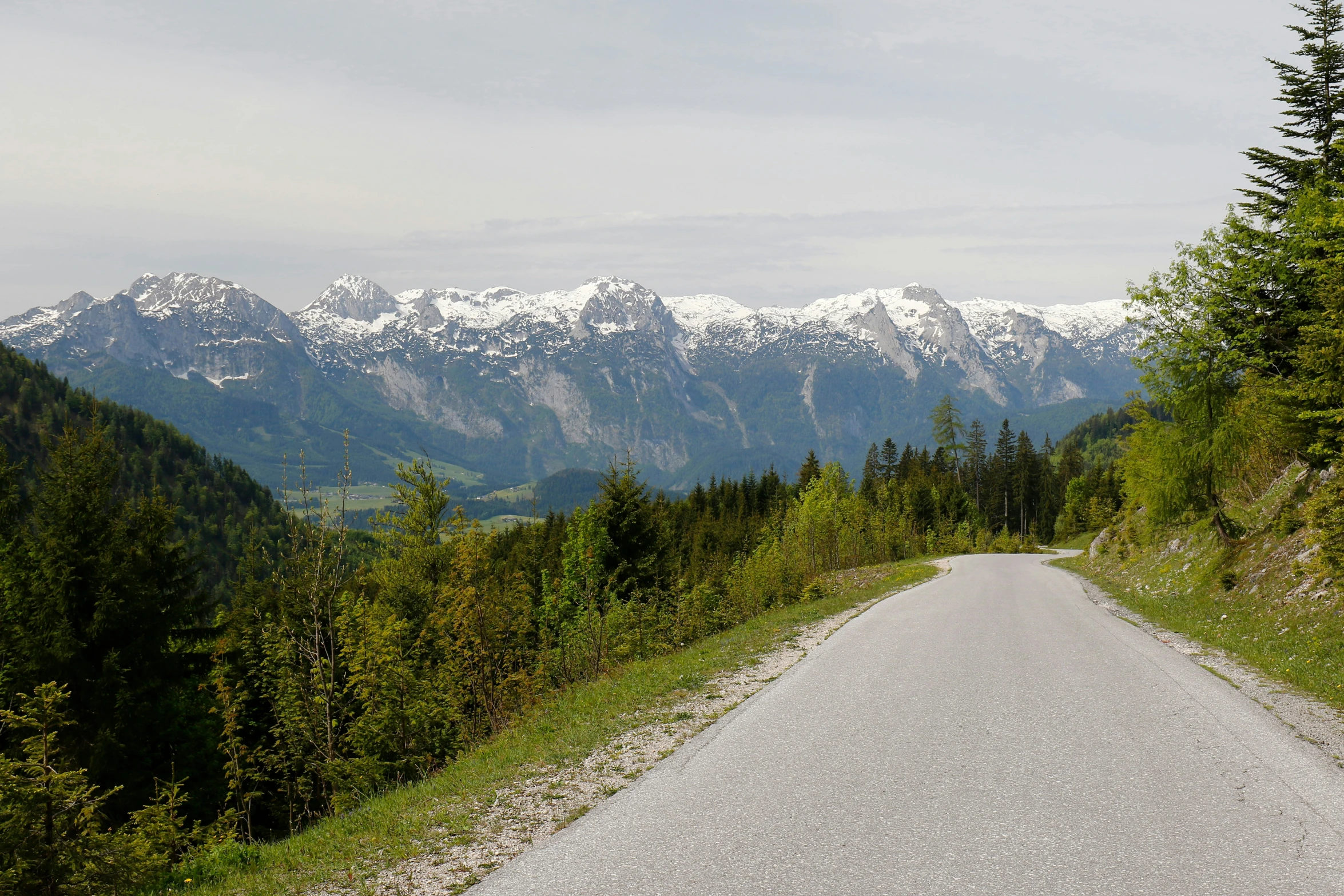 a long, winding road through the mountains with snow capped mountains