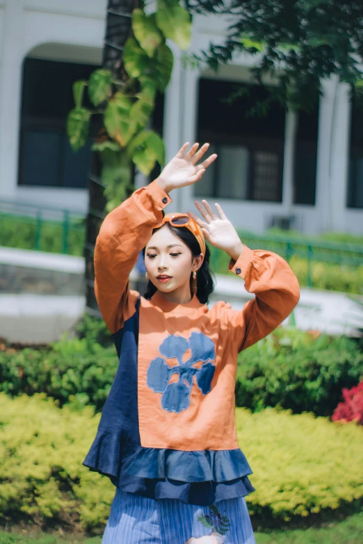 a girl in an orange sweater holds her hands in the air
