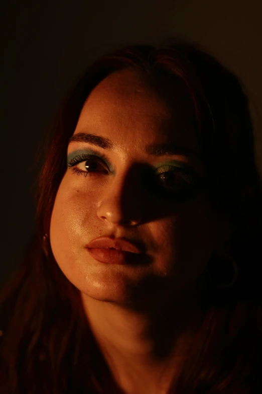 a woman with long dark hair has green eyeliner and a smoky, glowing shadow