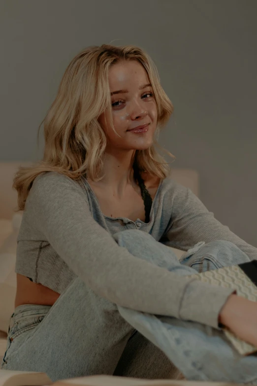 a blonde haired woman in a sweater sits on the floor and looks up at the camera