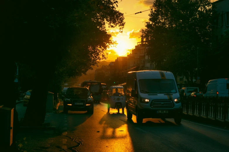 the sun sets on a street with traffic, vehicles, and pedestrians