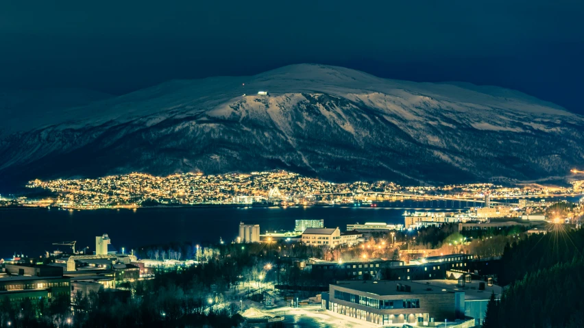 snow covered mountain at night next to small town