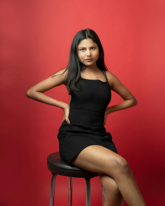a woman posing on a stool in front of a red background