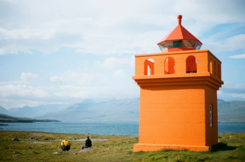 a yellow tower on the top of a hill with two people standing around