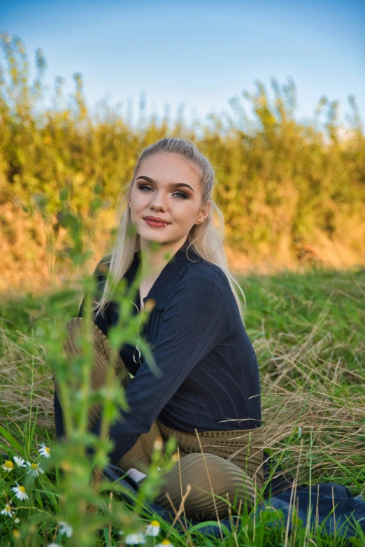 a woman with blonde hair sitting on the ground next to tall grass