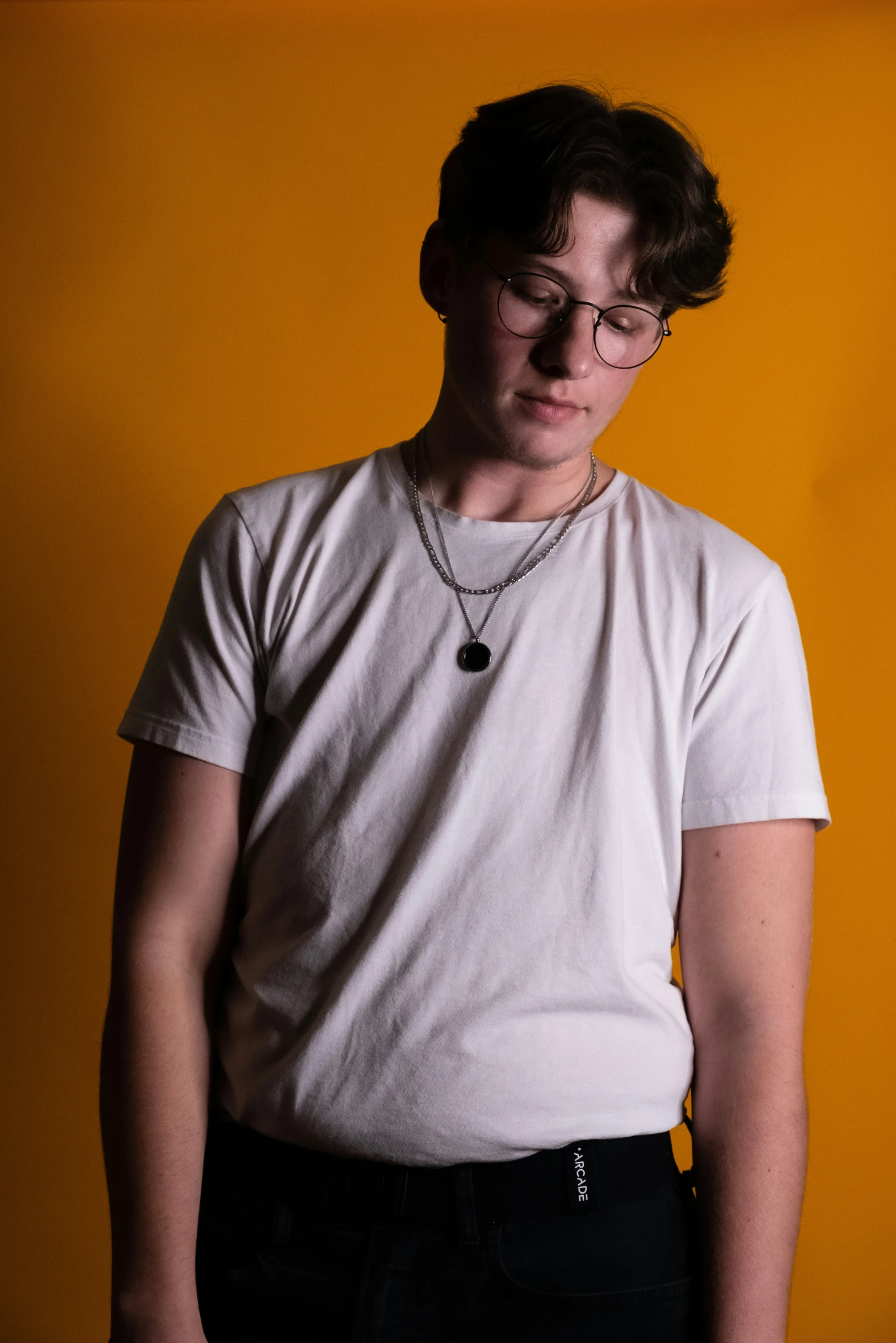 a boy with glasses standing against a yellow wall