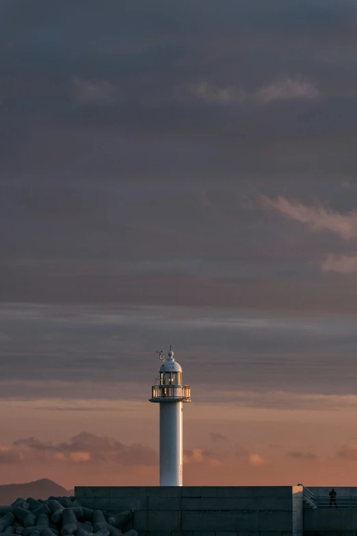 a person walks toward a lighthouse as the sun sets