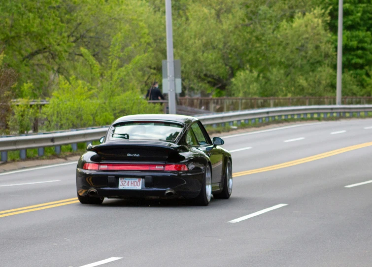 a porsche 911 on a highway with lots of trees in the background