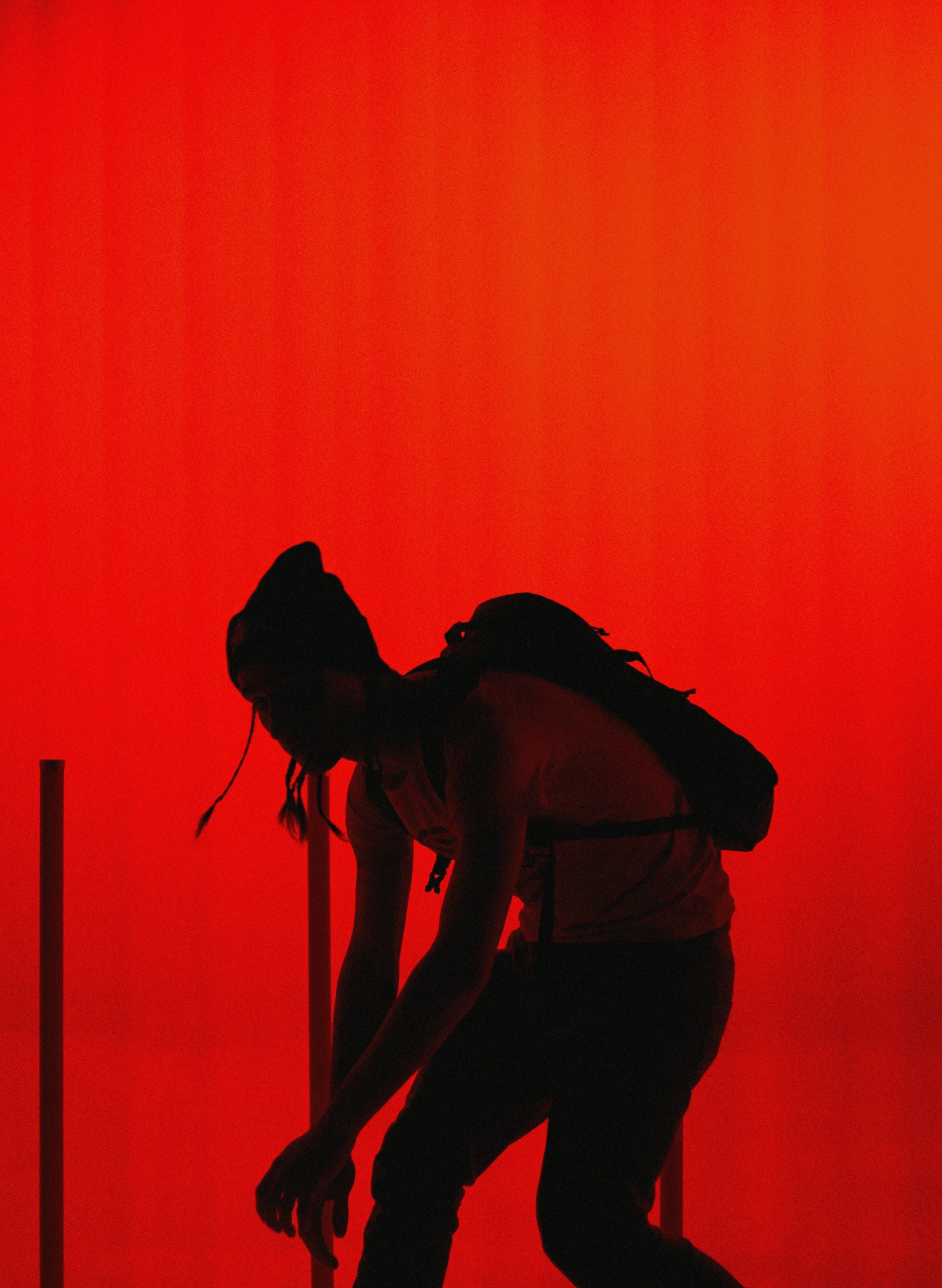 a silhouetted person climbing up a pole in front of red light