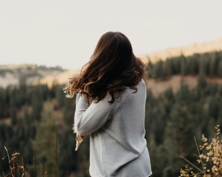 woman in white sweater and tan pants standing next to a mountain