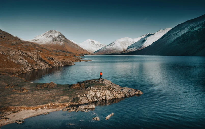 the lone person stands on top of the mountain, surrounded by snow covered mountains