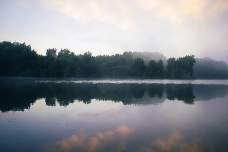 a lake with a few trees on the other side and clouds in the sky