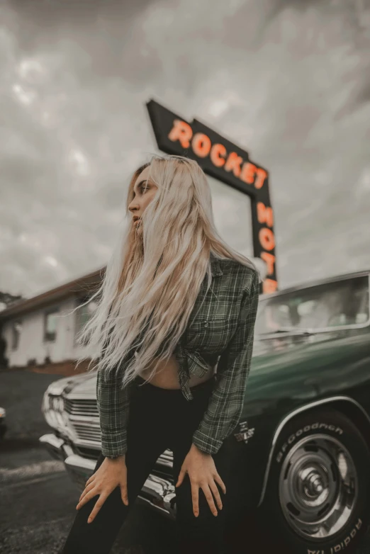 a blonde woman sitting on a car in front of rockstard