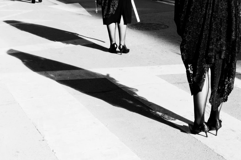 a woman in dress walking on sidewalk next to another person