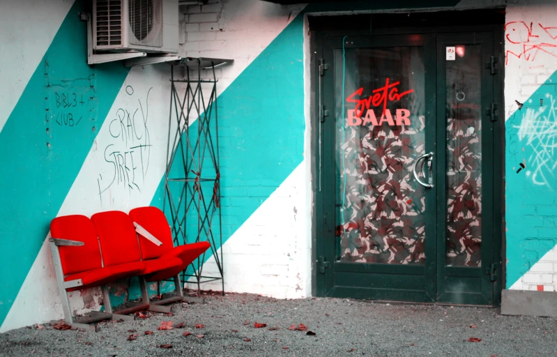 a red bench on the sidewalk in front of a green door