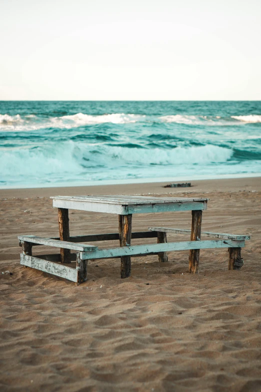 a picnic table sits in the sand near a water wave