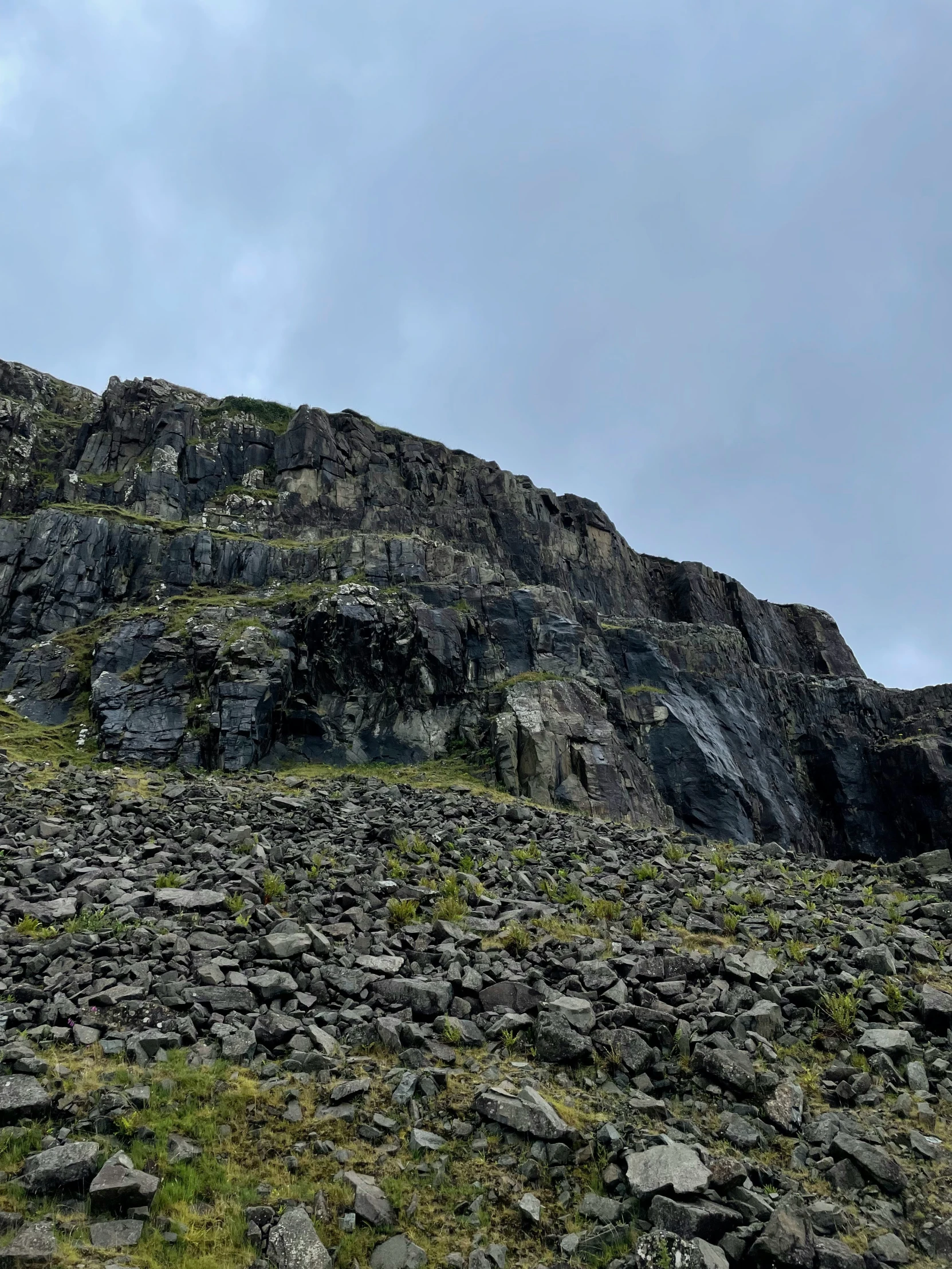 a mountain with grass and rocks, and blue sky in the background