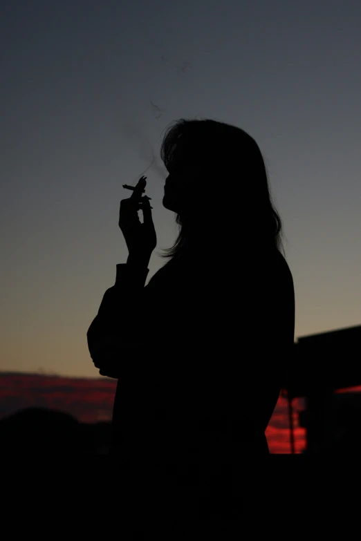 woman smoking a cigarette in the sunset with a view of buildings