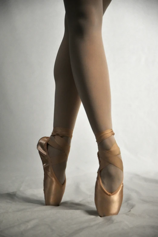 the legs and ankles of a ballet dancer in shiny gold ballet shoes