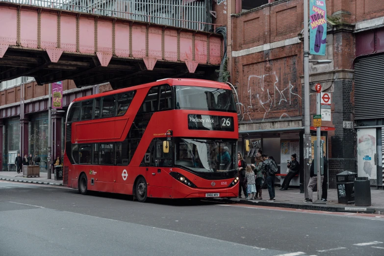 a double decker red bus parked at the side of the street in front of pedestrians