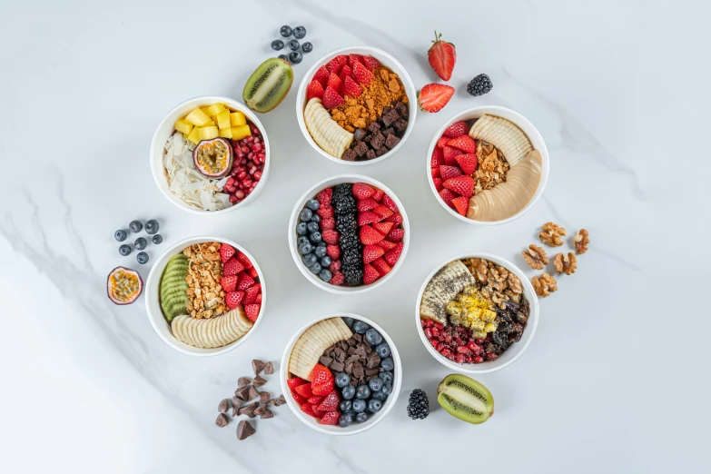 seven cups filled with fruit, cereals and nuts arranged on top of a marble surface