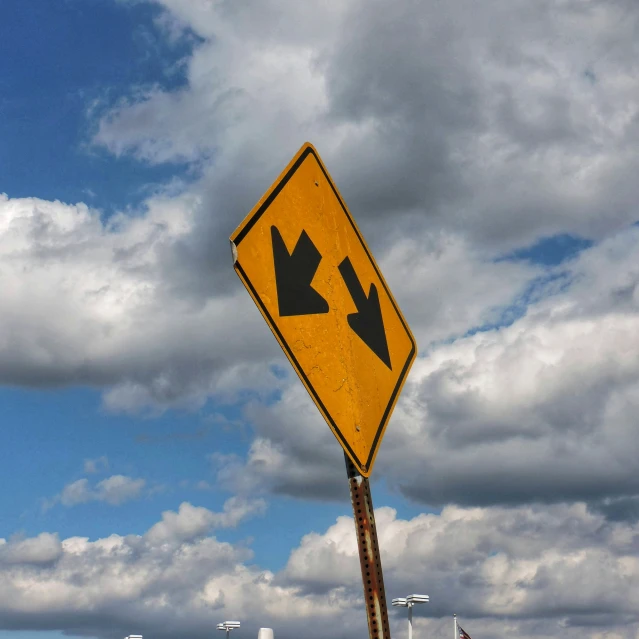yellow and black arrow sign with cloudy blue sky in background