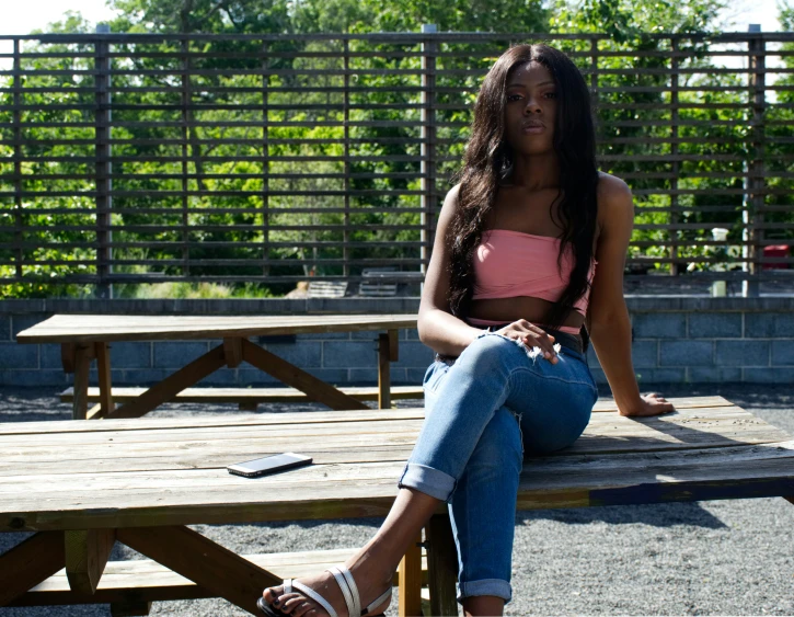 a girl with an unoned  and jeans sits on a picnic table