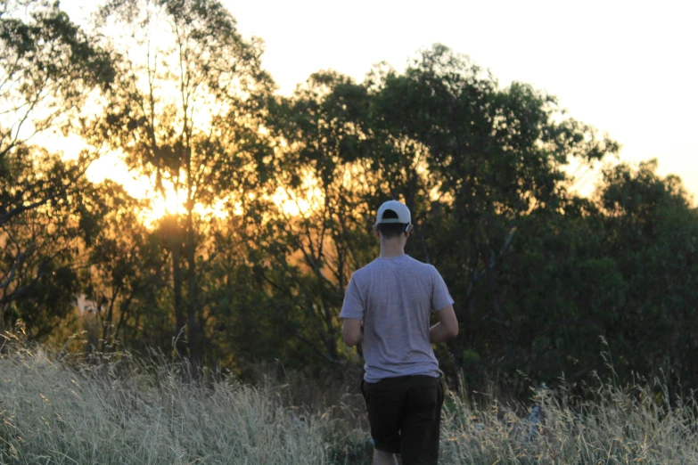 a man walks through tall grass towards the setting sun