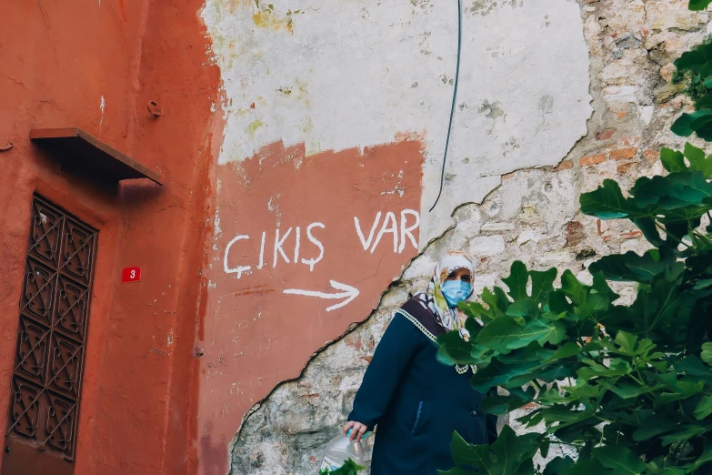 the person in the blue coat is standing near a graffiti covered wall