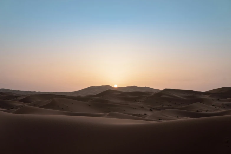 an expanse of sand dunes and a sunset in the background