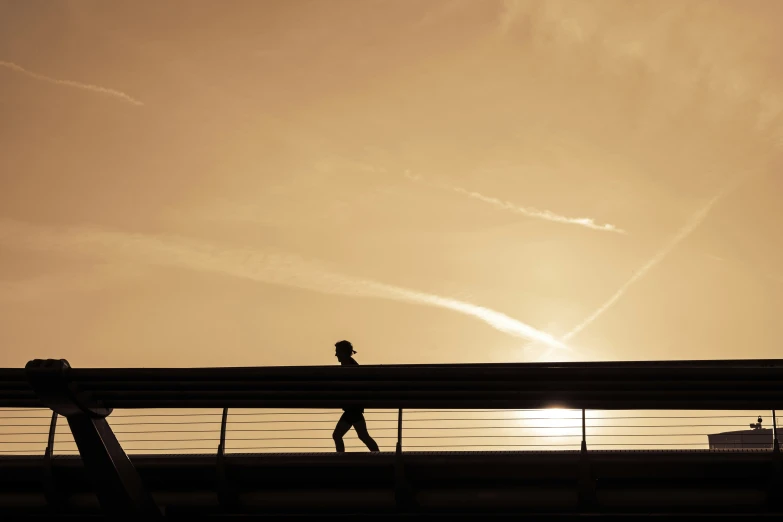 two people walk over a bridge at sunset