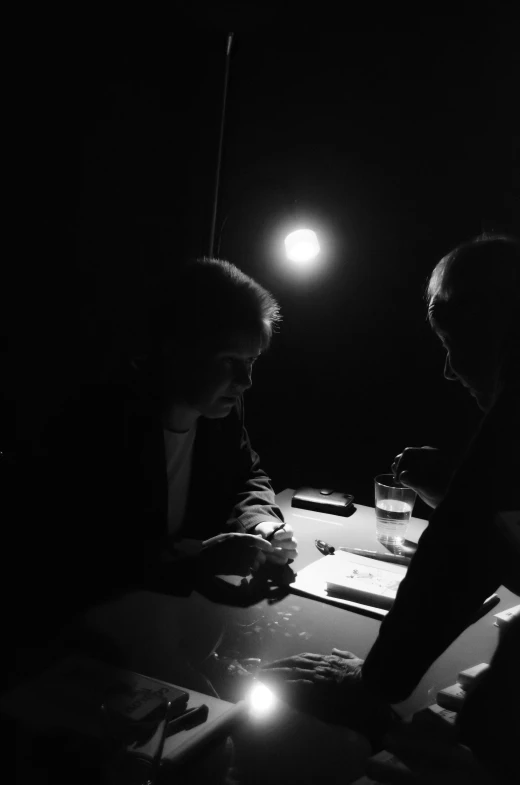 two men at a table with an object and one man is typing on a cell phone