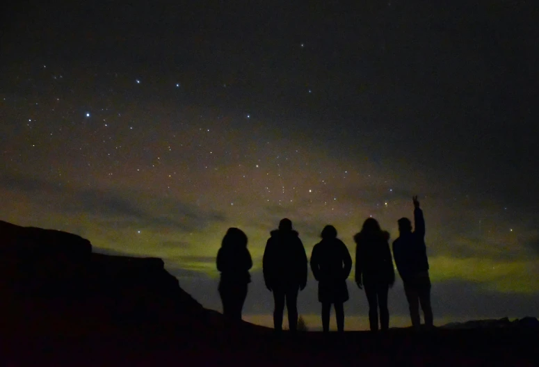 three people stand under a dark sky at night