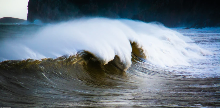 a crashing wave crashes in front of a rock formation