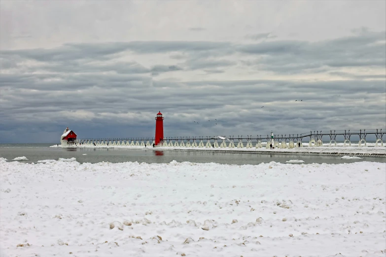 an empty snowy beach with a light house near the water