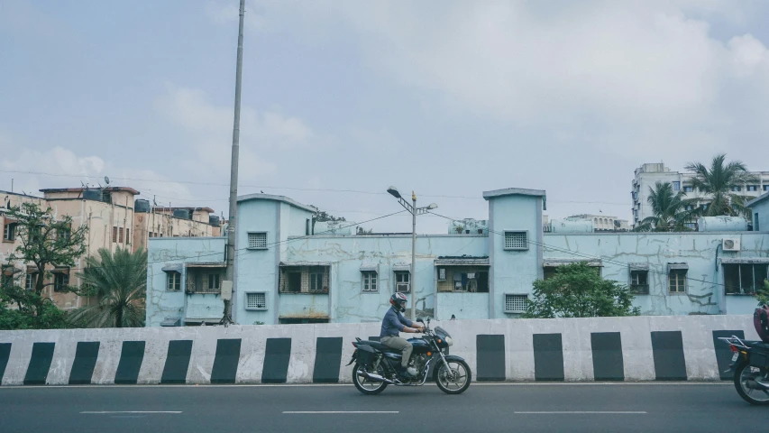 two motorcyclists are riding past old blue buildings