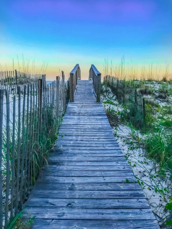 a boardwalk leading to the beach with a sunset in the background