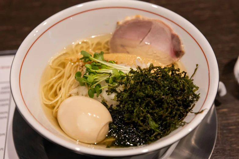 a bowl with noodles, meat, and greens on a table