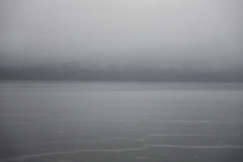 the plane is flying over the water in the cloudy weather