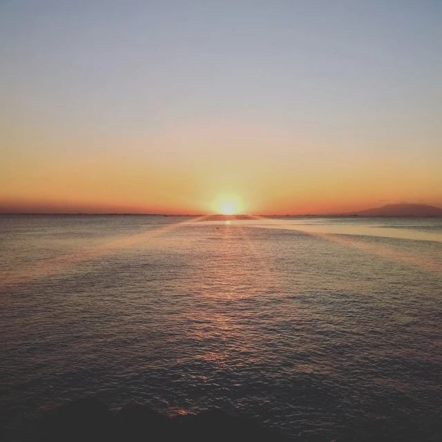 the sun is setting over the ocean and the boat is going by