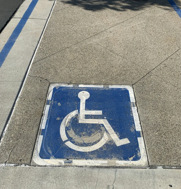 a handicap sign is on the sidewalk of a busy street