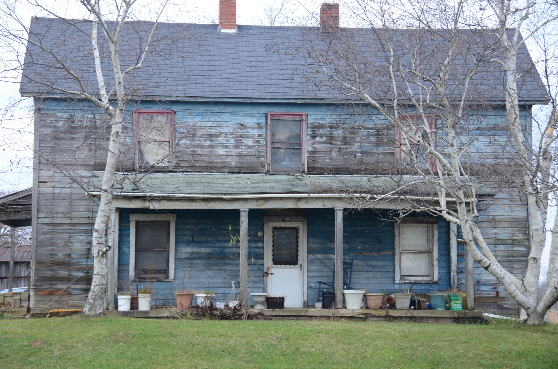 a blue old house with several pots on the porch