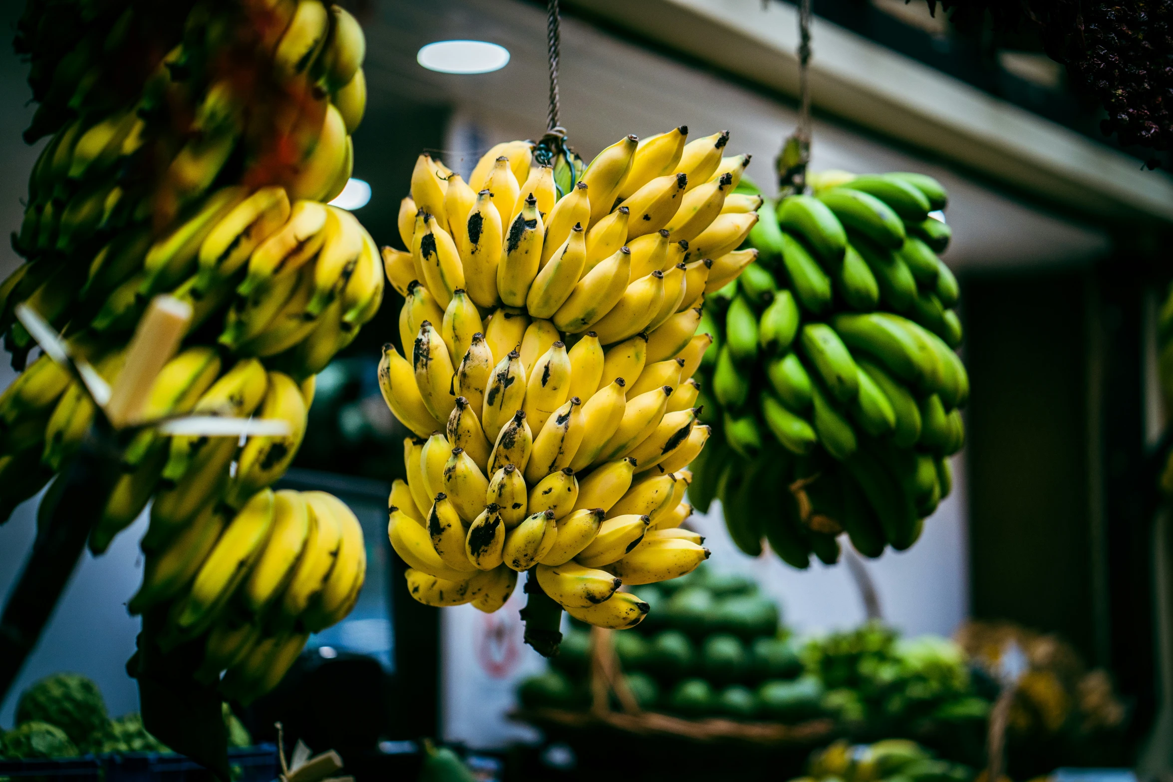 several bananas hanging up in a store filled with fresh produce