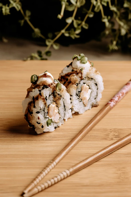 two chopsticks laying on the wooden surface with some sushi in it