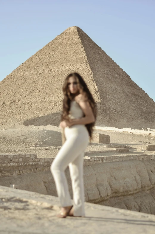 a woman standing on a sand ground with a pyramid in the background