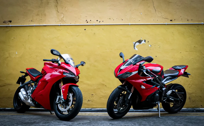 two motorcycles parked outside by a yellow wall