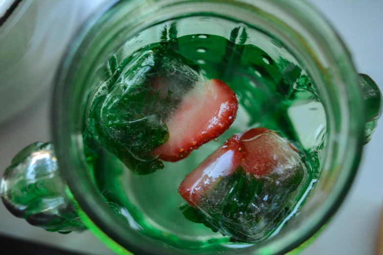 two strawberries and one piece of leaf sitting in a jar