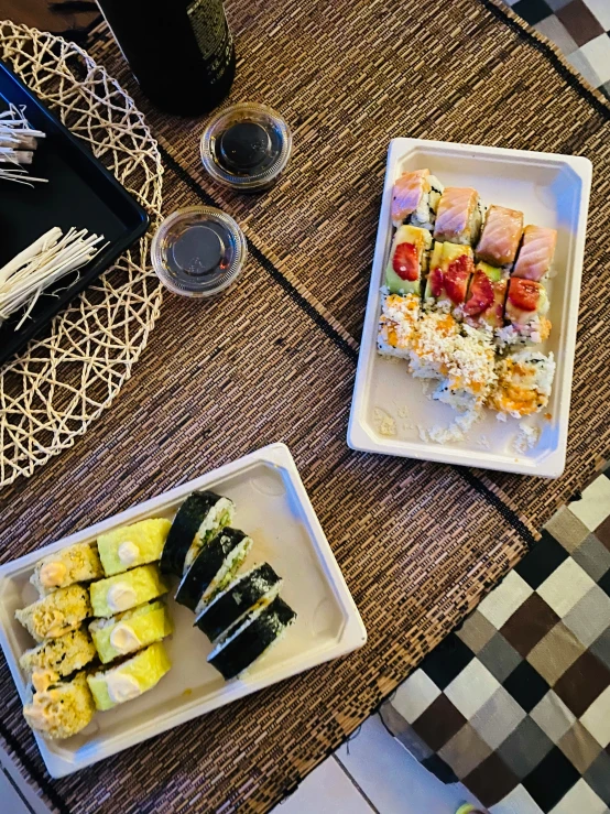 three plates are set on a woven placemat at the table, including different kinds of sushi and chop sticks