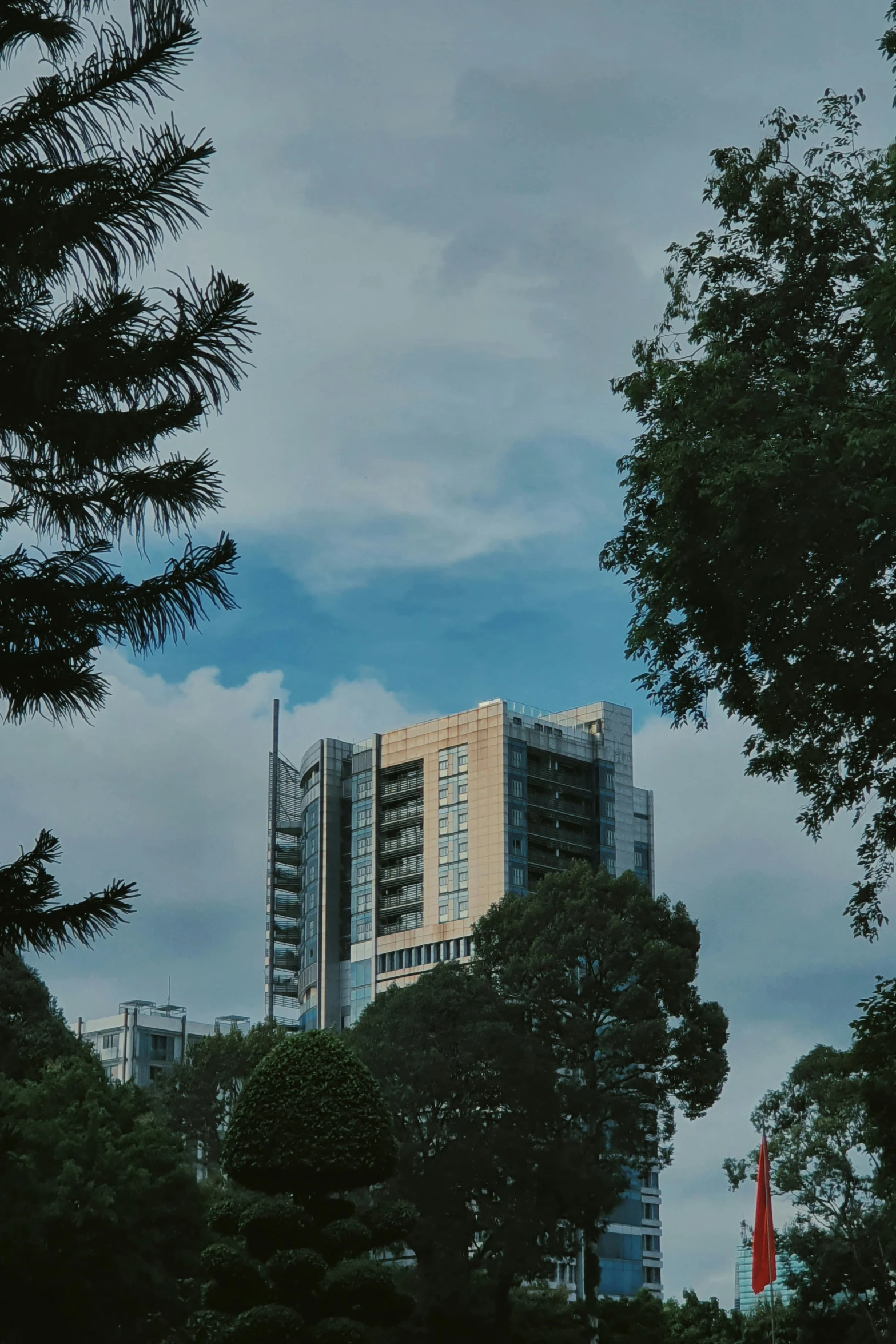 two tall buildings stand among green trees against a blue cloudy sky