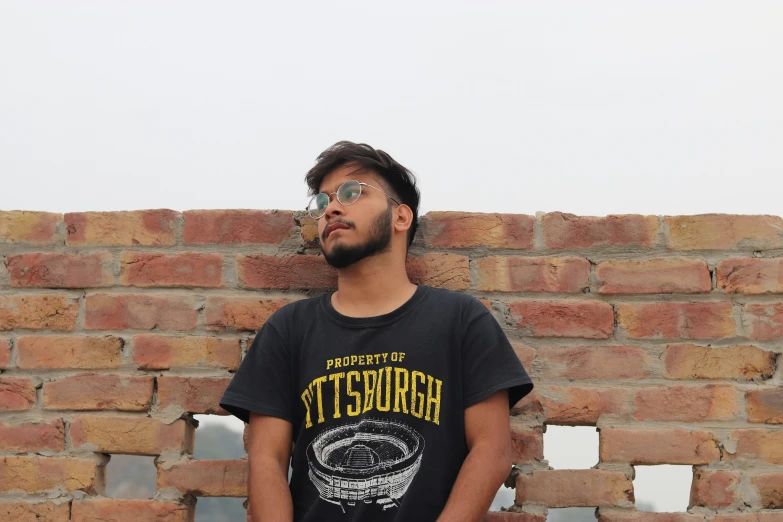 a man wearing glasses is standing next to a brick wall